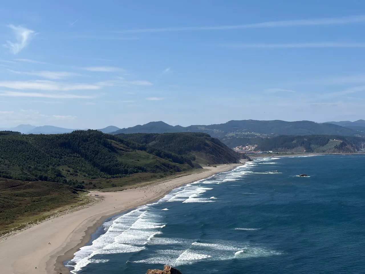 A long sandy beach and green headlands on the Asturias coast, in the north of Spain, under a clear sky